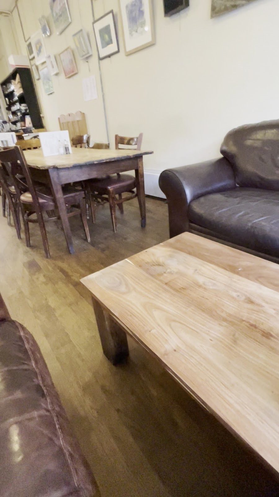 Seating area with two brown leather sofas around a light wood coffee table, a long dark wooden table with chairs behind, and framed pictures hung along the wall.