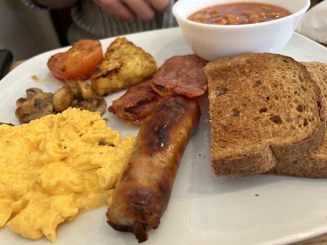 Close view of a cooked breakfast with scrambled egg, sausage, bacon and beans.