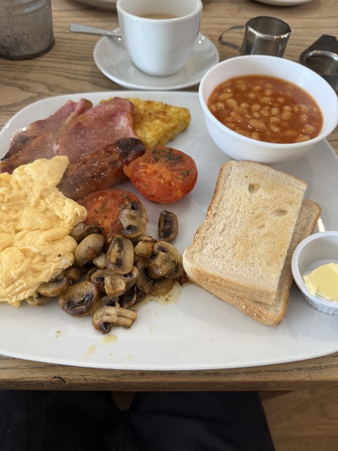 Breakfast plate with beans, toast and butter, a cup of tea and a small milk jug on a wooden table.