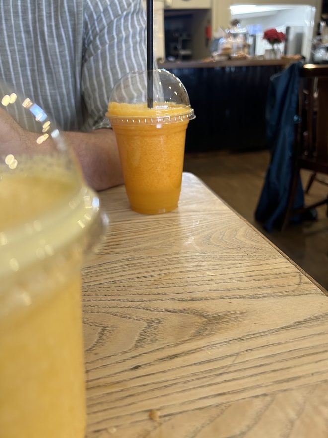 Orange juice on a wooden table with the counter and a vase of flowers out of focus behind.