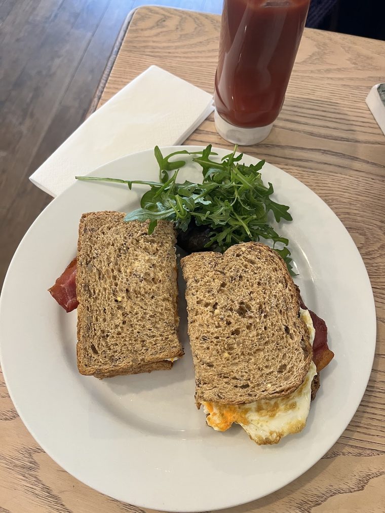 Bacon and fried egg sandwich on granary bread, halved, served with rocket.