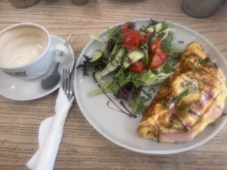 Ham omelette with chives on a plate with dressed salad leaves, tomato and cucumber.