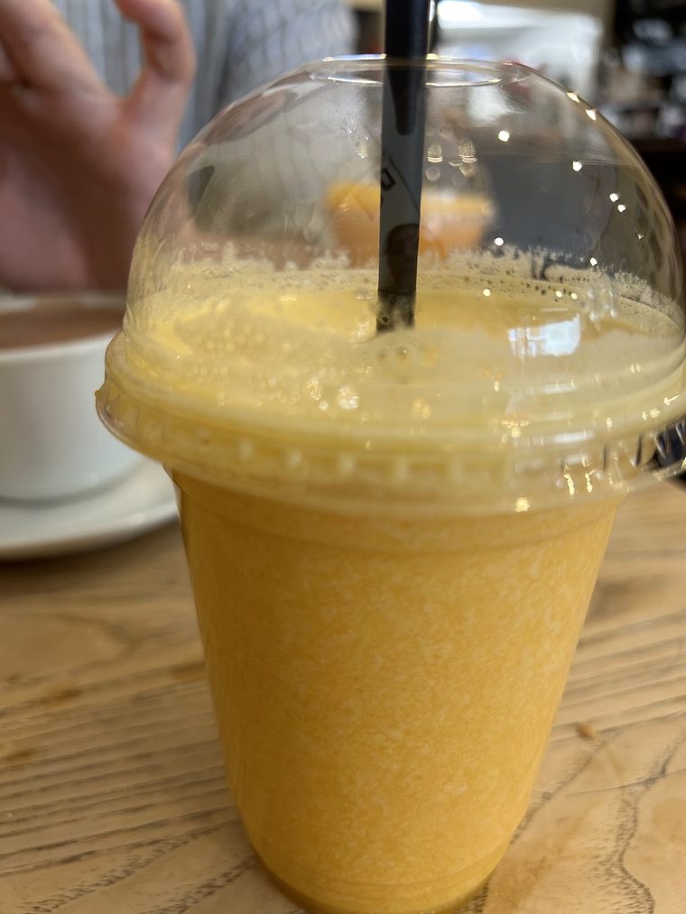 Fruit smoothie in a clear cup with a domed lid and straw.