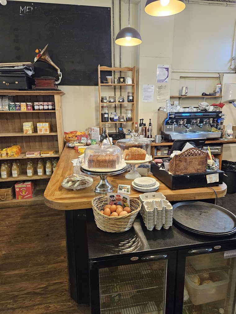 Two cakes on the counter, one sliced under a glass dome and one topped with crumble on a cake stand.
